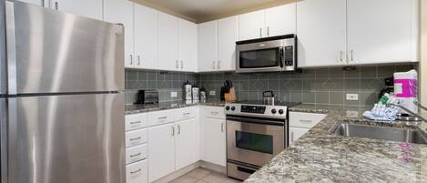 A modern kitchen with stainless steel appliances, white cabinets, and a granite countertop.
