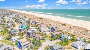 A coastal residential area with houses along the beach, clear skies, and a view of the ocean.