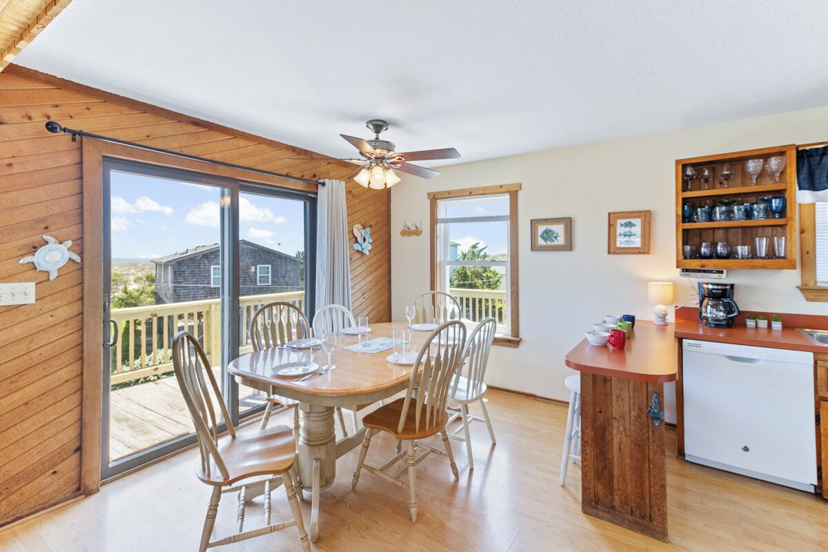 A cozy kitchen with a wooden island, a dining area with chairs, and a view of a house through the sliding glass doors.