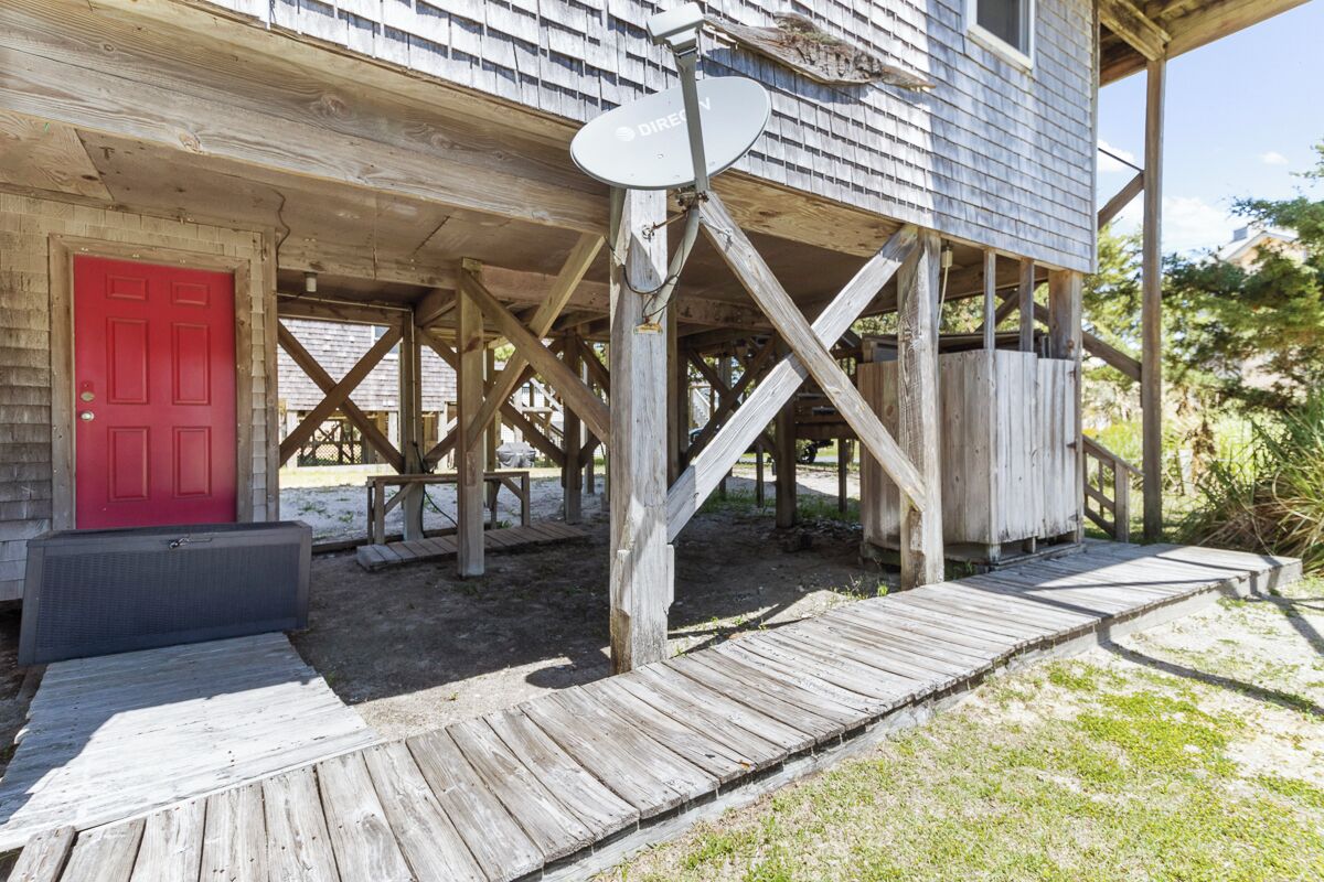 A rustic wooden building with a red door, a satellite dish, and a wooden deck.