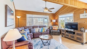 A cozy living room with a brown leather sectional sofa, a wooden entertainment unit, and a ceiling fan.