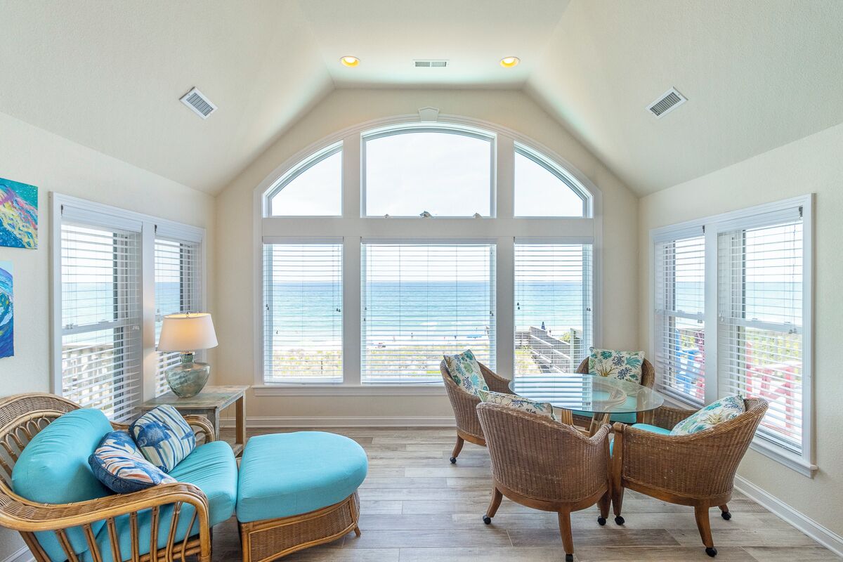 A sunlit room with a large arched window, wicker furniture, and a glass table.