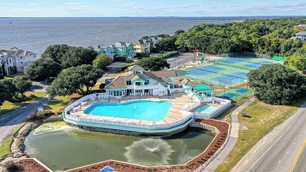 En stor swimmingpool omgivet af en terrasse, tennisbaner og havudsigt.