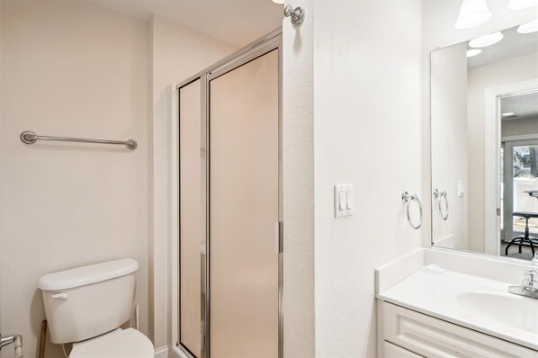 Une salle de bain comprenant des toilettes, une douche avec une porte en verre, un lavabo avec un miroir et un porte-serviettes.