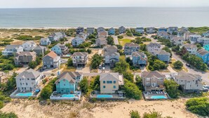A coastal residential area with houses, some with swimming pools, and a beach in the background.