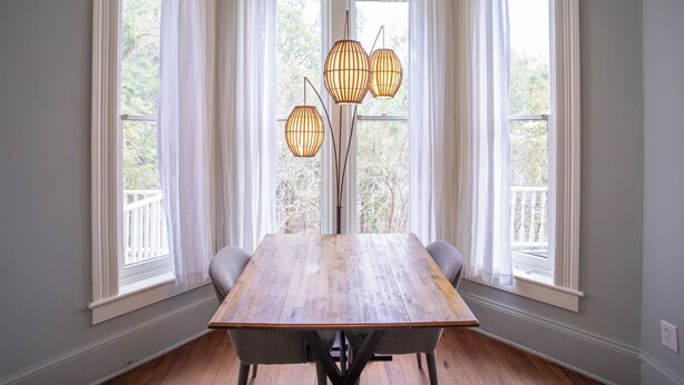 Un comedor con una mesa de madera, cuatro sillas y una lámpara de pie alta con múltiples luces.