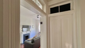 Un pasillo con una puerta blanca, una chimenea, un sofá gris y un ventilador de techo.