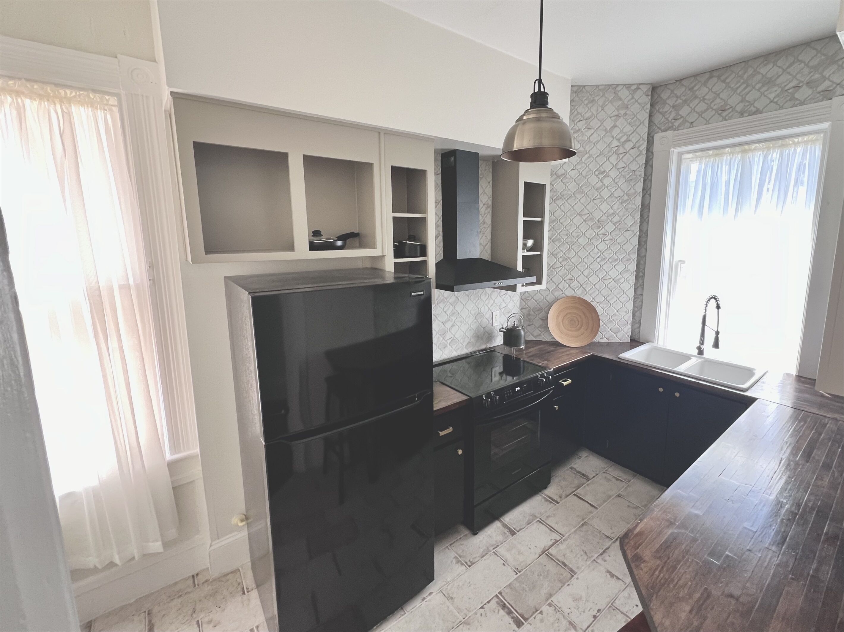 Een moderne keuken met een zwarte koelkast, inbouwmeubels, een houten aanrecht en een hangende pendelverlichting.