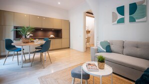 Una sala de estar moderna con un sofá gris, una mesita redonda y un comedor con mesa y sillas de madera.