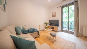 Una sala de estar moderna con un sofá, un televisor, una mesita y vistas al verdor exterior.