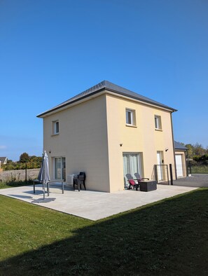 A two-story house with a flat roof, a covered patio area with outdoor furniture, and a fenced yard.