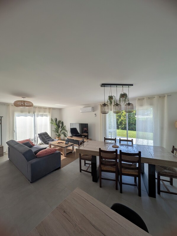 A modern living room with a sofa, dining table, chairs, and a TV. - Gîte plage de Normandie Asnelles plage du débarquement Gold Beach (Calvados)