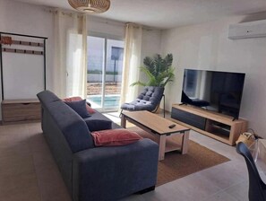 Moderni olohuone, jossa on sohva, nojatuoli, televisio ja liukuovet, jotka johtavat parvekkeelle.