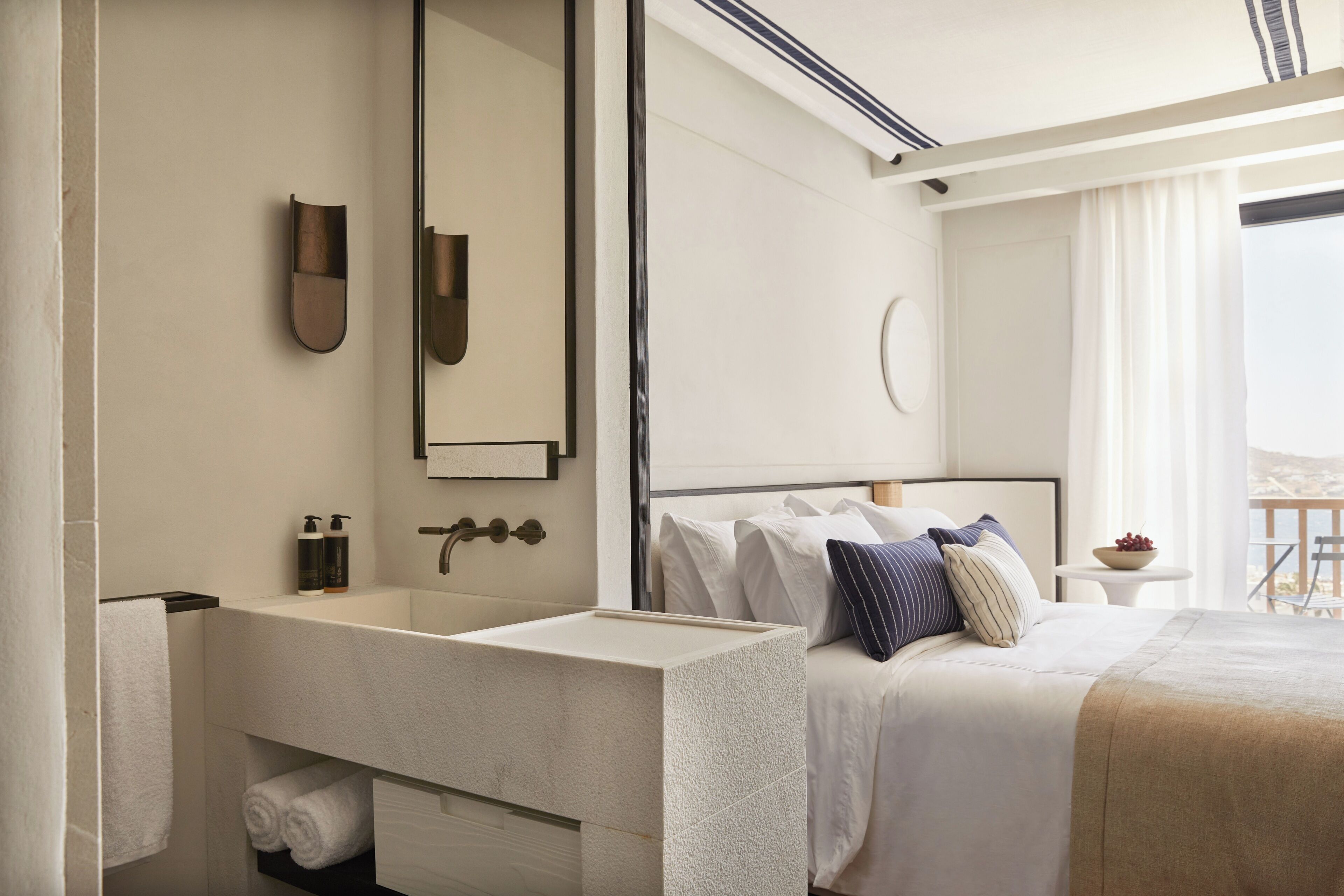 Une chambre d’hôtel moderne dotée d’un grand lit, d’une coiffeuse intégrée, d’un grand miroir et offrant une vue sur l’extérieur.