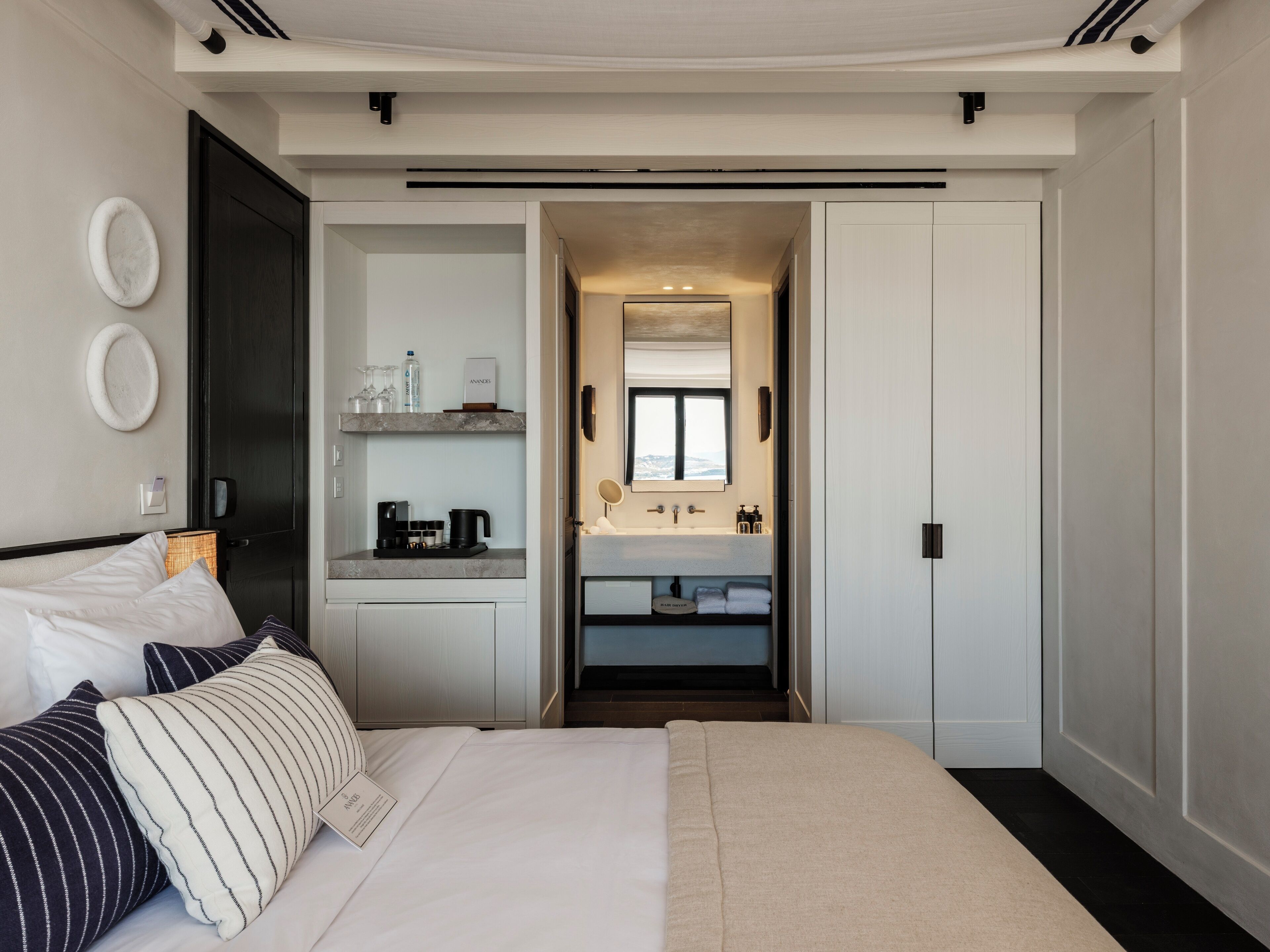 Ein modernes Hotelzimmer mit großem Bett, Nachttisch, integriertem Schreibtisch, Badezimmer mit Waschbecken und Spiegel sowie Bergblick durch das Fenster.