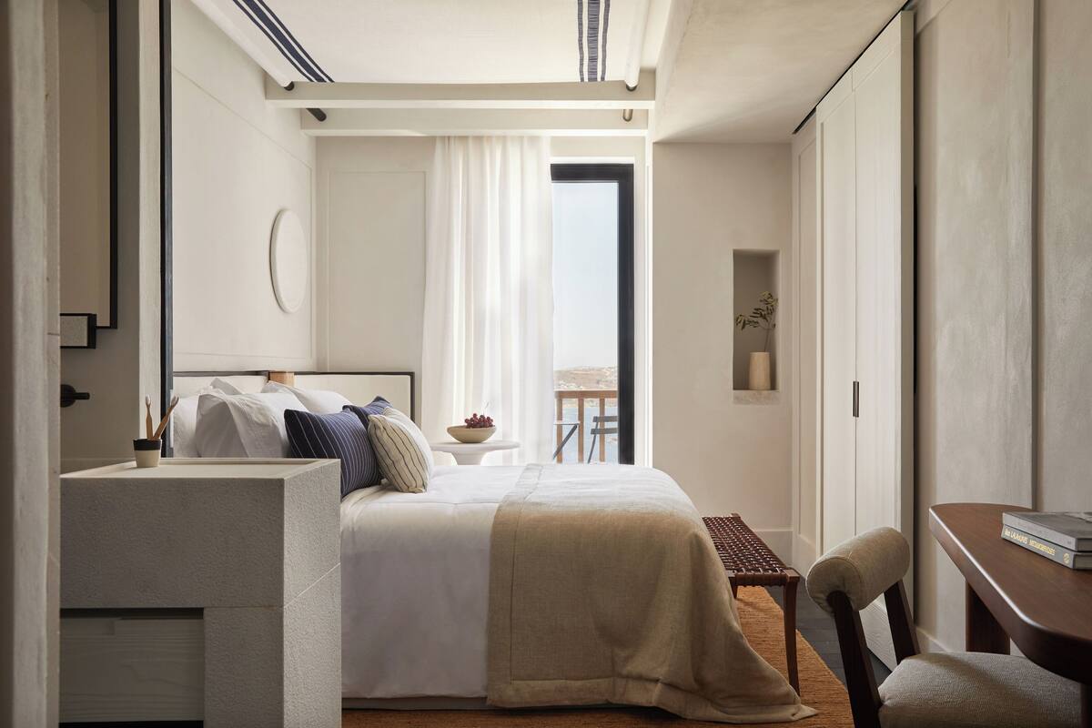 A modern hotel room with a bed, bedside table, chair, and a view of the outdoors.