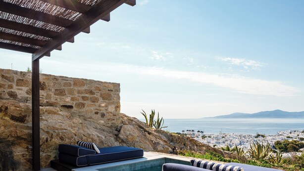 Un muro de piedra, una piscina y vistas a la playa y las montañas.