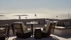 Un espacio al aire libre iluminado por el sol con vistas al mar, que incluye sillas de mimbre, una mesa redonda y un sofá.