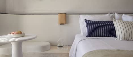 A modern hotel room with a bed, a round table with a plate of fruit, a wall-mounted lamp, and a round mirror.