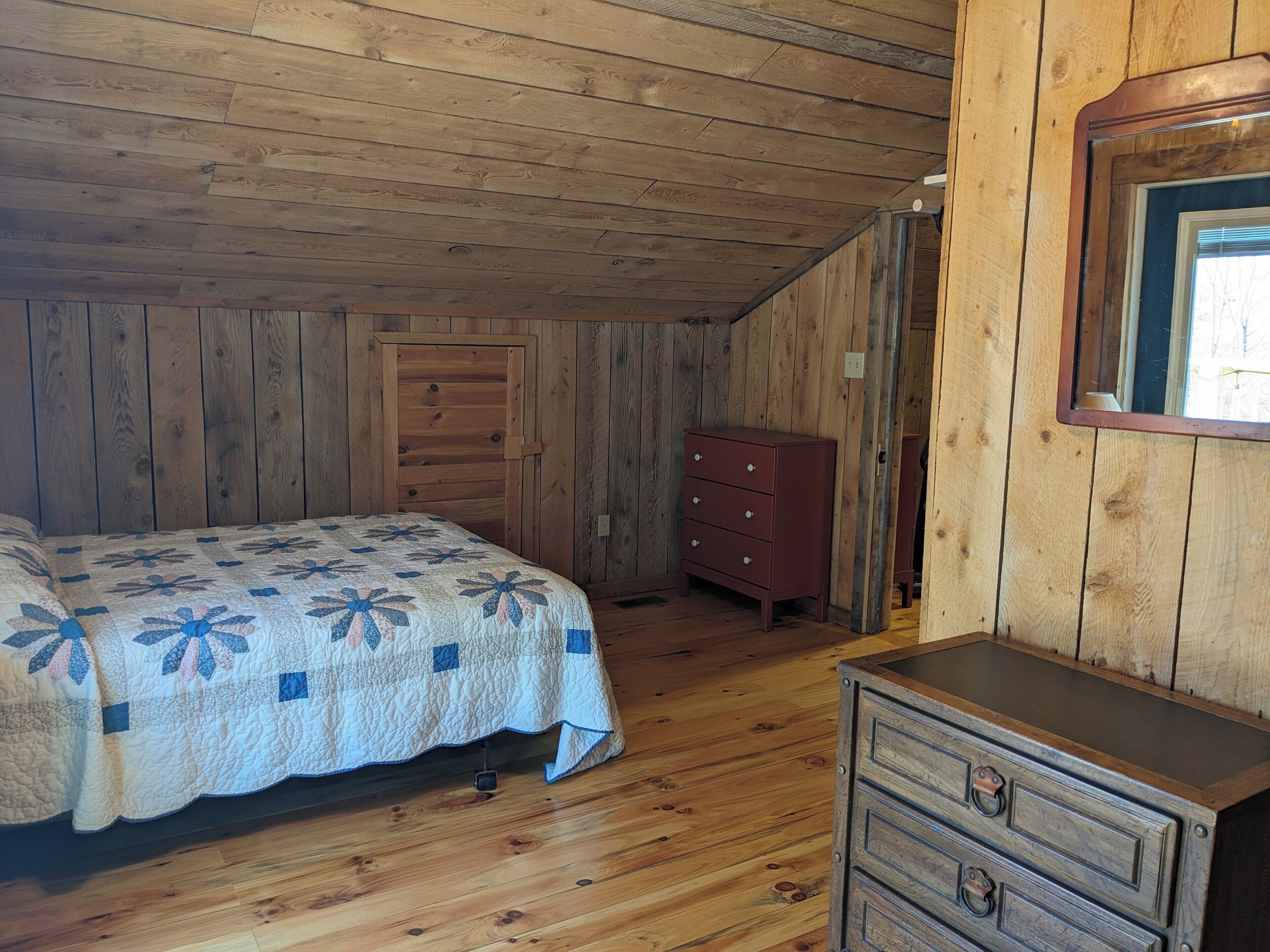 A wooden-paneled room with a bed, a dresser, and a mirror.