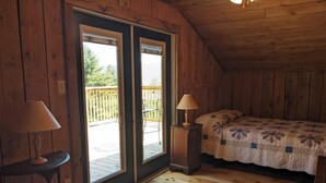 Et soveværelse i en træhytte med en seng, to sengeborde, en lampe og en skydedør til en terrasse.