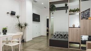 A modern, minimalist living space with a dining area, a sofa, and a TV mounted on the wall.