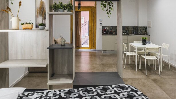 A modern living room with a black and white patterned rug, a wooden bench, and a dining area with white chairs.