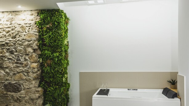 Ein modernes Badezimmer mit einer Steinsäule, einem vertikalen Garten und einer Badewanne.