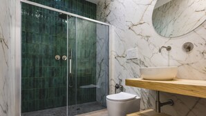 Ein modernes Badezimmer mit einer gläsernen Duschkabine, einer marmorierten Wand, einem weißen Waschbecken und einem hölzernen Waschtisch.