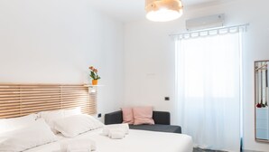 A modern hotel room with a large bed, a bedside table with a vase of flowers, a sofa, and a large window with sheer curtains. - 4bnb - Reale House Borgo (Rome)