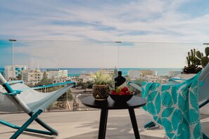 A balcony with a view of the sea, a table with a bottle and a bowl of fruit, and two hammocks. - Protaras Eden Seaside Suite (Paralimni)