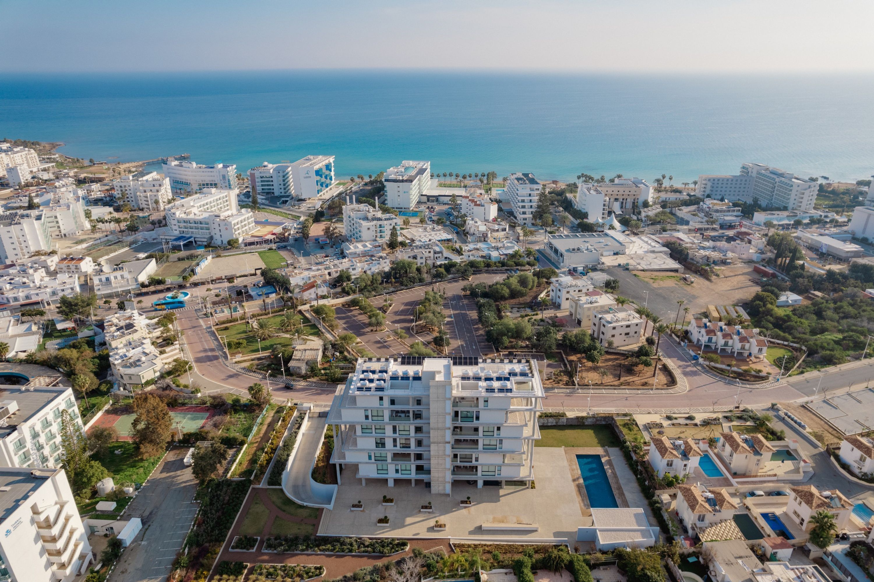A coastal cityscape with modern buildings, a central plaza, and a large pool.