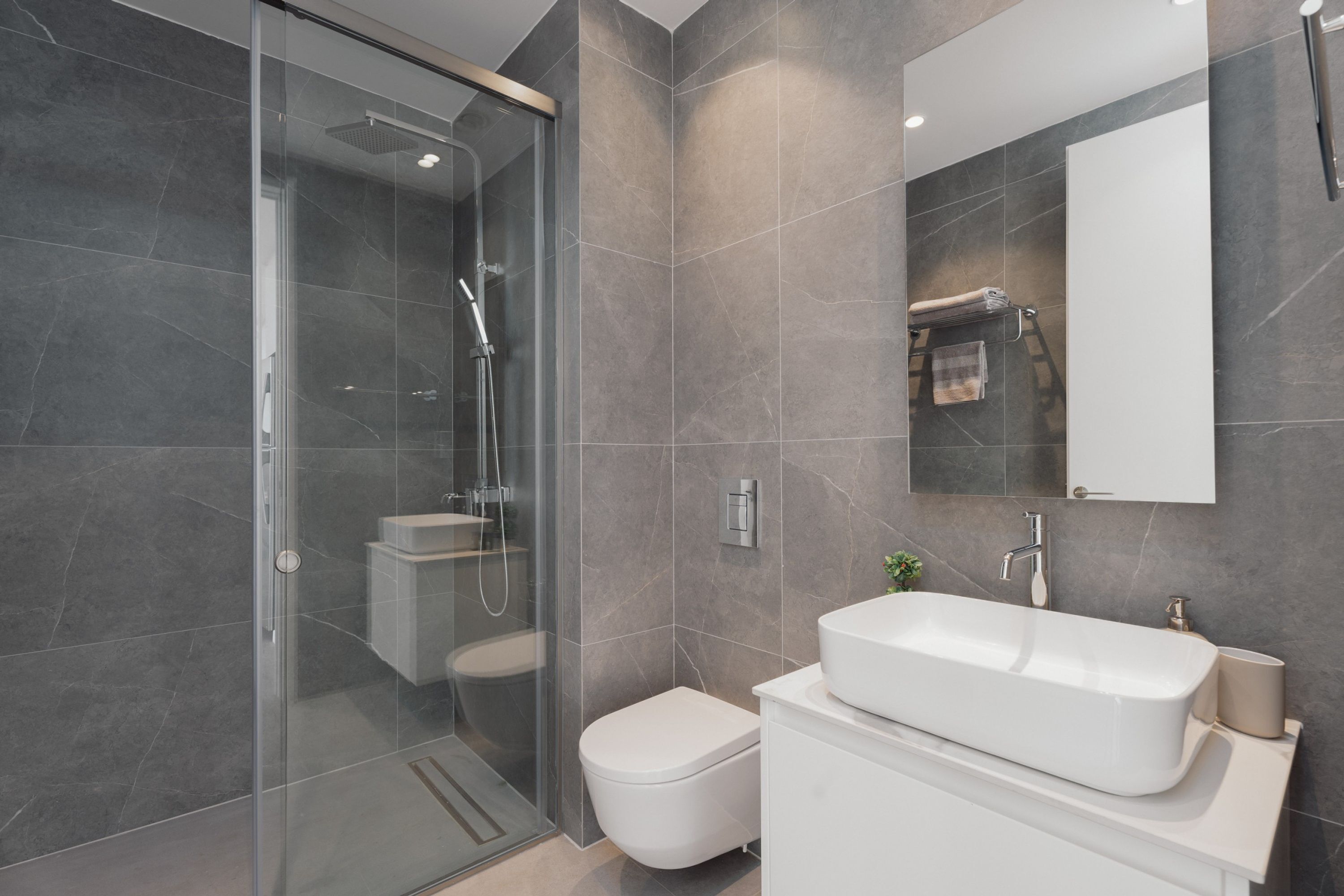 Un baño moderno con ducha envuelta en vidrio, inodoro blanco y un lavamanos grande con un espejo encima.