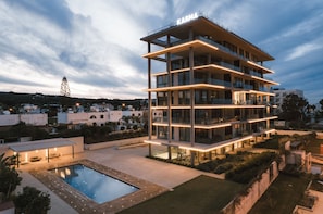 A multi-story hotel with a pool, outdoor lighting, and a view of the surrounding area. - Protaras Eden Seaside Suite (Paralimni)