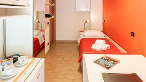A compact hotel room with a bunk bed, a microwave, a small table with a magazine, and a bright orange accent wall.