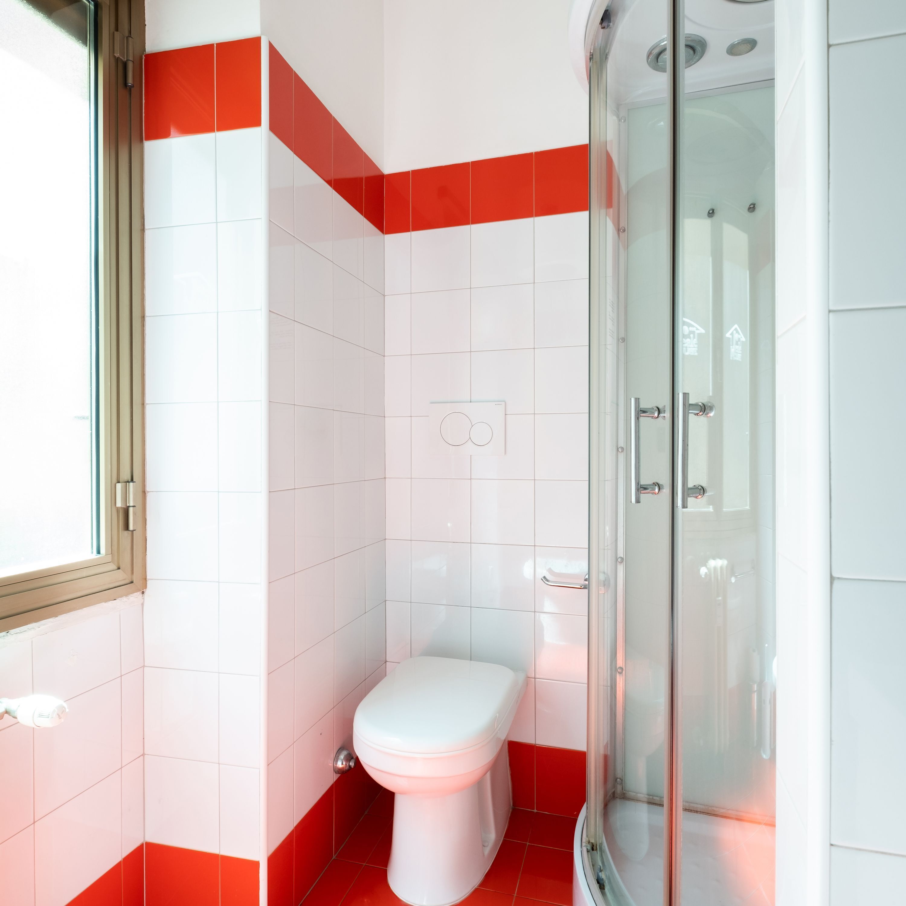 A bathroom with a toilet, a glass shower enclosure, and red and white tiled walls.