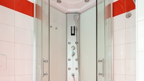 A modern shower enclosure with a glass door, a control panel, and a handheld showerhead.