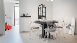 Un comedor con una mesa redonda, sillas transparentes y una ventana con marco negro.