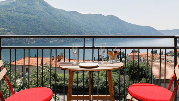Un balcón con una mesa dispuesta para dos, con vistas a un lago y montañas.