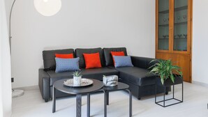 Un salón moderno con un sofá de cuero negro, cojines estampados en rojo y azul, dos mesas de centro negras y un mueble grande de madera con puertas de vidrio.