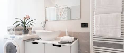 A modern bathroom with a washing machine, a large sink, a towel rack, and a mirror.