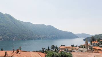 A coastal town with terracotta-roofed buildings, a prominent church tower, and a lake surrounded by hills.