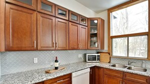 A kitchen with wooden cabinets, a granite countertop, a microwave, a wine bottle, and a dishwasher. - Blue Mountain Gem (R) near the Village (Town of Blue Mountains)