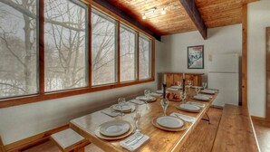 A dining area with a long wooden table set for a meal, large windows, and a wooden ceiling. - Blue Mountain Gem (R) near the Village (Town of Blue Mountains)