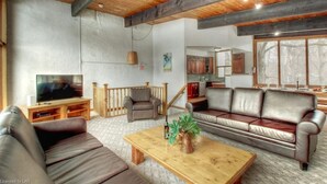 A living room with a TV, leather sofas, a wooden coffee table, and a kitchen in the background. - Blue Mountain Gem (R) near the Village (Town of Blue Mountains)