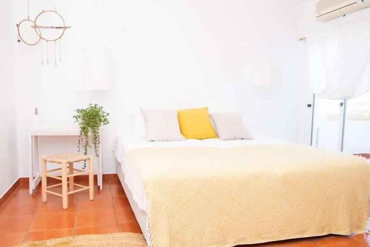 A bedroom with a bed, a bedside table, a chair, a hanging plant, and a window with curtains.