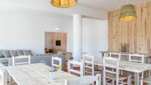 A dining area with rustic wooden tables and chairs, a grey sofa, and a wooden accent wall. - Utopia (Aljezur)