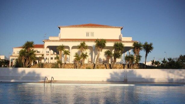 A hotel with a swimming pool, palm trees, and a clear sky. - Utopia (Aljezur)