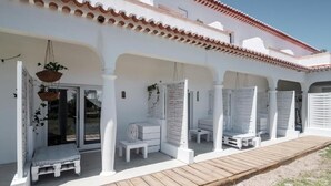 A covered outdoor seating area with white furniture and a wooden deck. - Utopia (Aljezur)