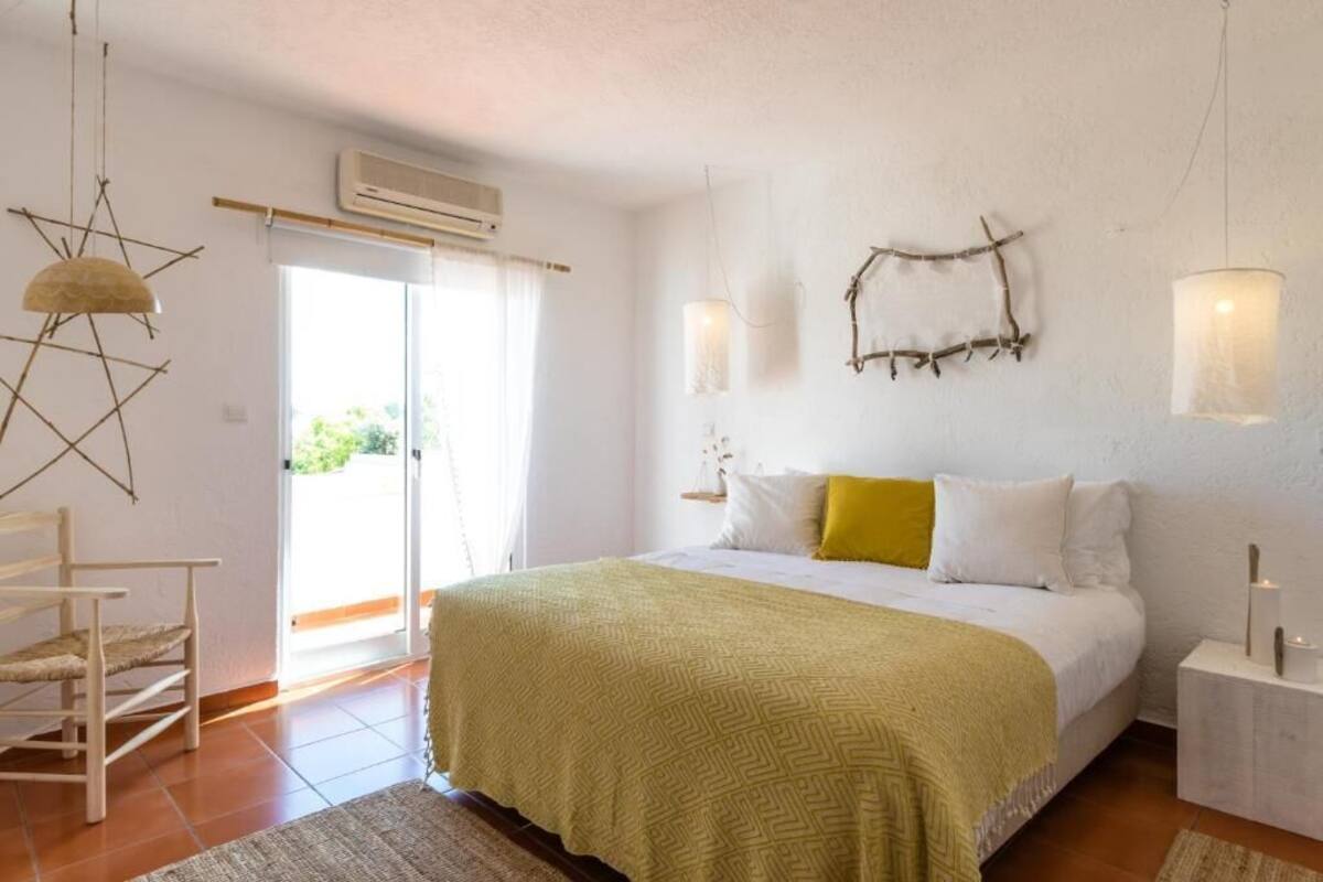 A bedroom with a bed, a chair, a wall-mounted light, and a window.